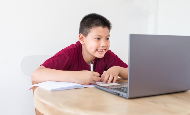 Asian boy studying online on computer laptop with smiling and happy face at home