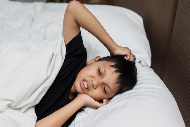 Asian boy suffering toothache and feel pain while lying on the bed