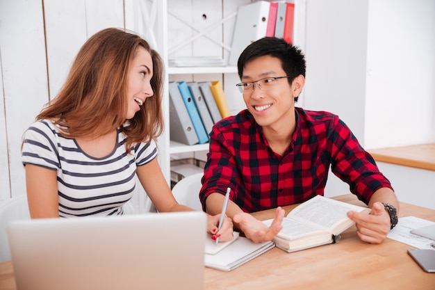 Asian boy wearing glasses and dressed in shirt in a cage and caucasian woman dressed in t-shirt in a strip print working together for project at classroom