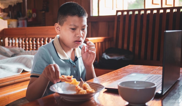 Asian boys eat junk food while sitting at a desk with notebooks and laptops at home