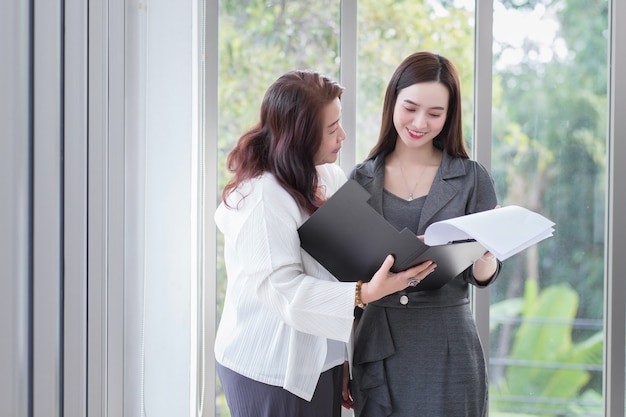 Asian business female stands and talk to another to consult about work intently in office.