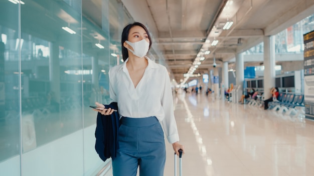 asian business girl using smartphone for check boarding pass walking with luggage to terminal at domestic flight at airport.