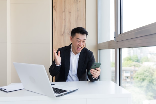 asian business man in office looking at mobile phone with emotion winner or win