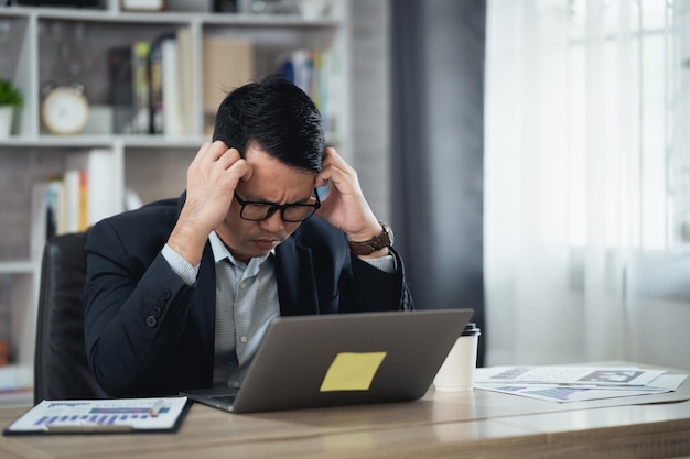 Asian Business man wear glasses and hand over head having stressful depression sad time while working on laptop at home Depression man sad serios working from home Working at anywhere concept