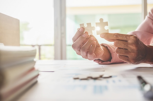 Asian business woman hands on a wooden office desk pick puzzle. Business solutions success and strategy concept. Businessman hand connecting jigsaw puzzle.Close up photo with selective focus.