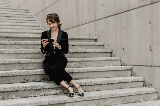 Asian business woman is smiling and sitting on stair. she is chatting with her boss