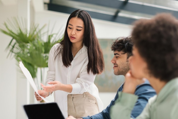 Asian business woman showing papers to colleagues working in office