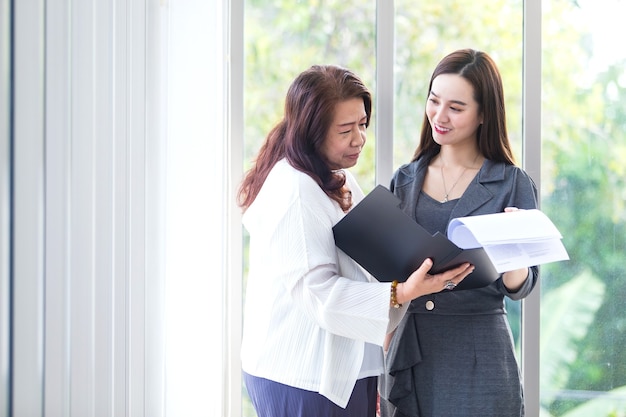 Asian business woman stands and talk to another to consult about work intently in office.