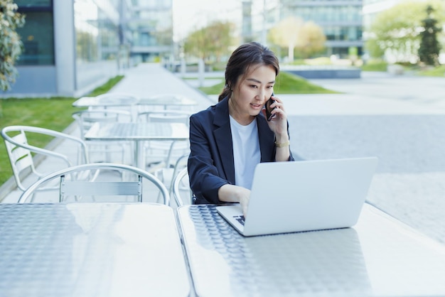 Asian business woman talking on phone and working with laptop outdoor