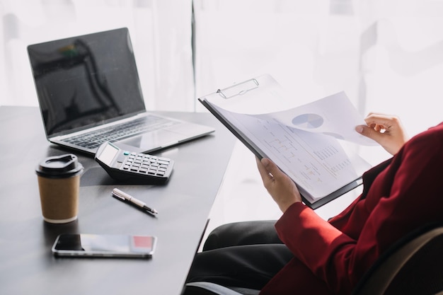 Asian Business woman using calculator and laptop for doing math finance on an office desk tax report accounting statistics and analytical research concept