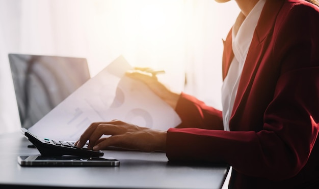 Asian Business woman using calculator and laptop for doing math finance on an office desk tax report accounting statistics and analytical research concept