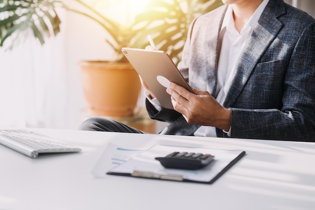 Asian Business woman using calculator and laptop for doing math finance on an office desk tax report accounting statistics and analytical research concept