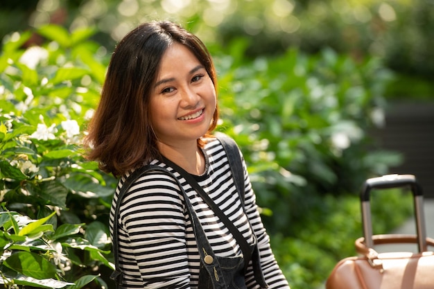 Photo asian business woman with yellow glasses sitting in the park with her suitcase in the background