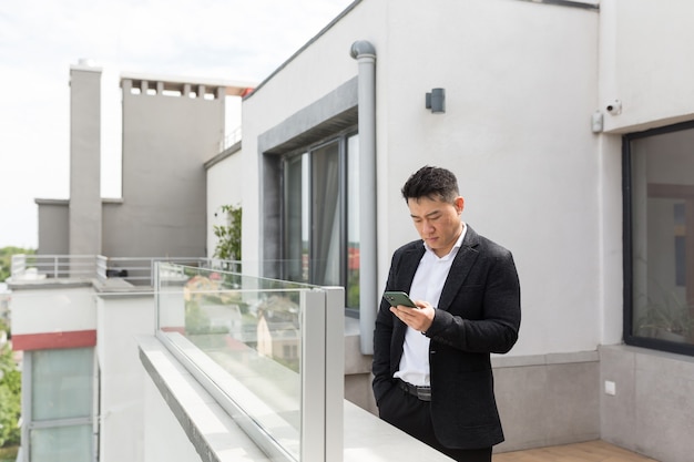 asian businessman in business suit enjoys phone standing on balcony terrace of modern office center