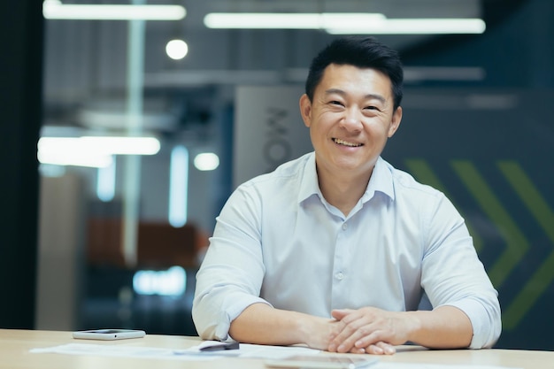 Asian businessman in modern office looking at webcam smiling sitting at table online meeting