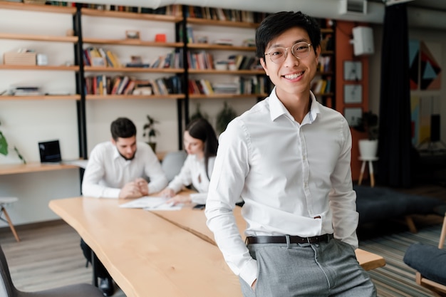 Asian businessman in office wearing glasses with coworkers on background