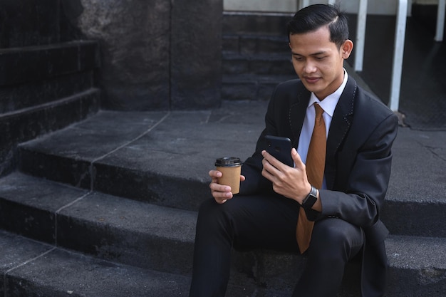 Asian businessman sitting while using cell phone and drinking coffee in the stairs