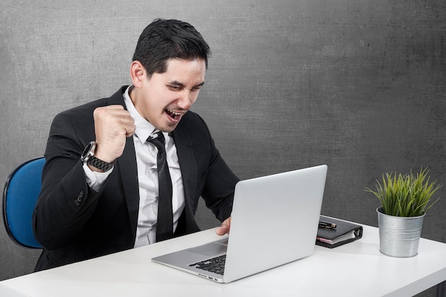 Asian businessman sitting with a laptop on the desk with a successful expression