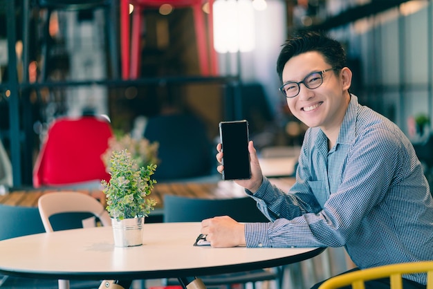 Asian businessman startup company entrepreneur sit smile with hand show smartphone happiness in new shop store office background business ideas concept