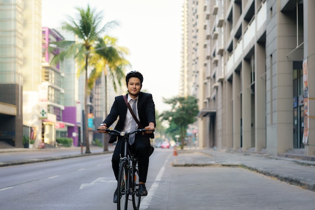 Asian businessman in a suit is riding a bicycle on the city streets for his morning commute to work