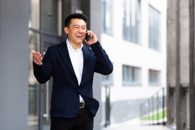 Asian businessman talking on the phone cheerful smiling reports good news near the office center outside