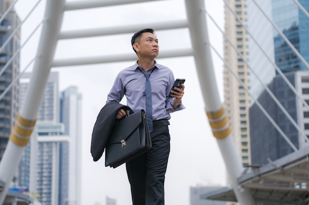 Asian Businessman walking and holding briefcase with business office buildings 