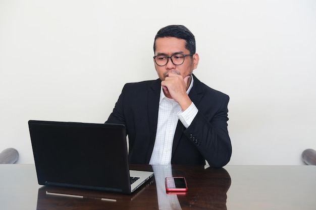 Asian businessman wearing black suit showing serious expression whne looking his laptop