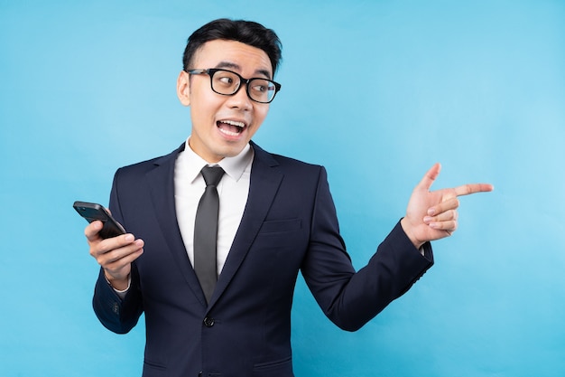 Asian businessman wearing suit holding smartphone on blue wall