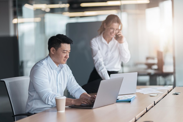 Asian businessman working on laptop with colleague in background