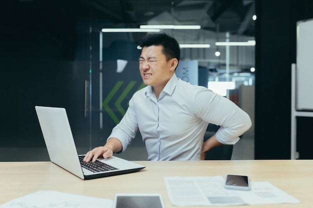 Asian businessman working in office having severe back pain overtired worker working with laptop