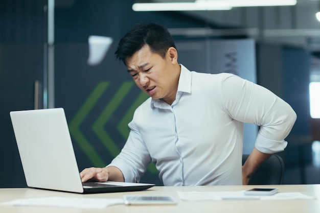 Asian businessman working in office having severe back pain overtired worker working with laptop