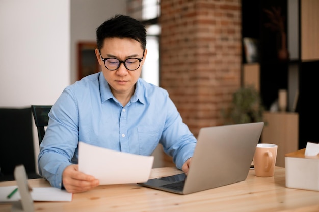 Asian businessman working with documents and laptop at home office checking financial papers sitting at workplace