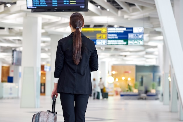 Asian businesswoman at the airport with trolley bag, near the flight display looking flight schedule