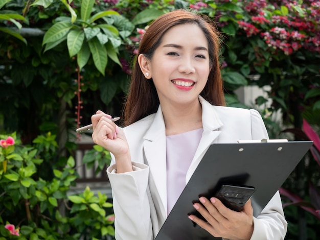 Asian businesswoman holding documents file standing outdoors. Smiling successful young businesswoman.