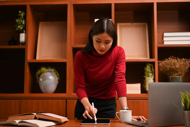 Asian businesswoman leaning on table working on her business project on digital tablet