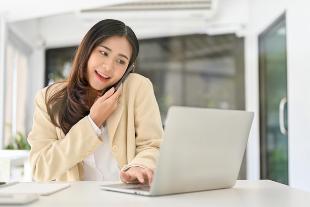 Asian businesswoman looking at details on the laptop screen while on the phone with a client