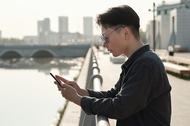 Asian businesswoman scrolling in smartphone by riverside