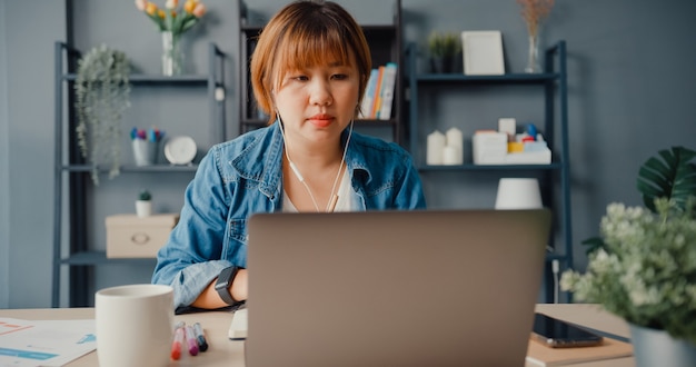 asian businesswoman using laptop talk to colleagues about plan in video call while working from house at living room