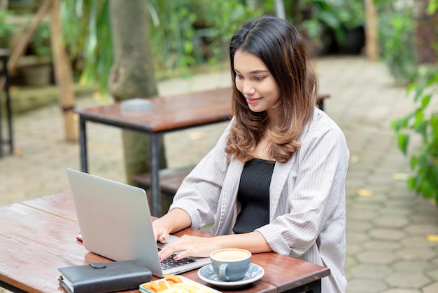 Asian businesswoman using a laptop with a mobile phone notebook and cup of coffee on the table