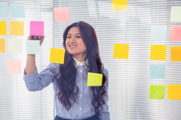 Asian businesswoman using sticky notes on wall in office