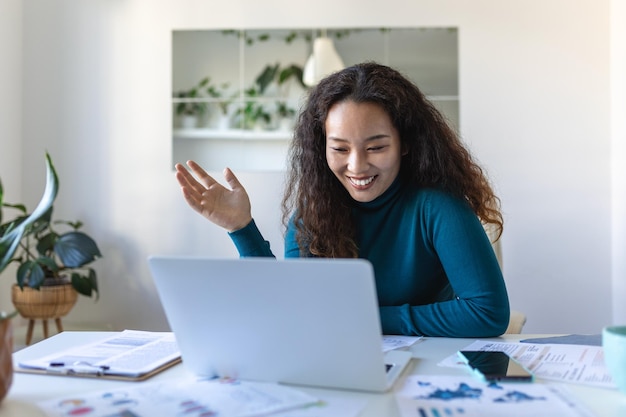 Asian businesswoman on a video call while sitting at her desk Shot of an attractive young woman using her laptop to make a video call at home