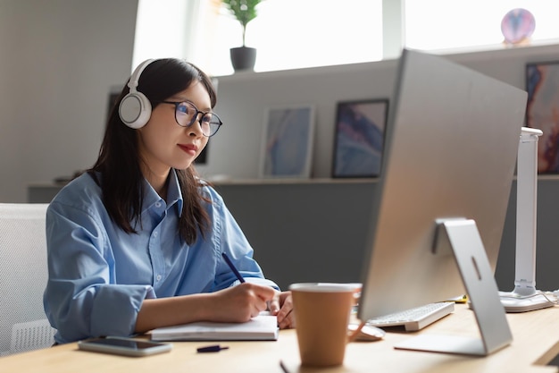 Asian Businesswoman Working On Computer And Taking Notes In Office