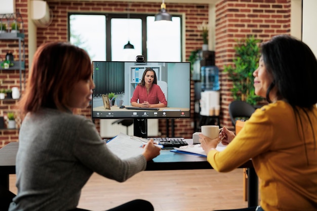 Asian businesswomen working at hiring appointment explaining job offer to remote applicant during online videocall meeting conference. Teleconference call on computer screen in startup office