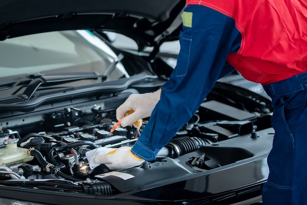 Asian car mechanic in an auto repair shop is checking the engine. For customers who use cars for repair services, the mechanic will work in the garage.