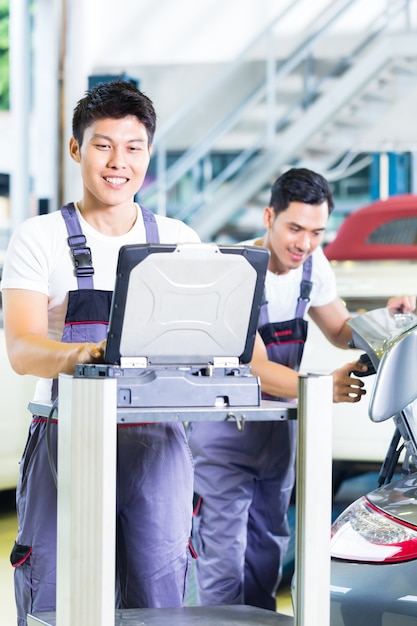 Asian car mechanics checking auto engine with diagnostics tool in his workshop