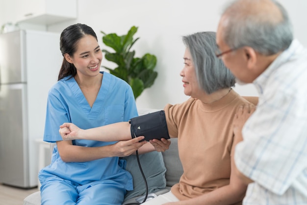 Asian caregiver doctor using digital pressure gauge measuring blood pressure of older woman patient