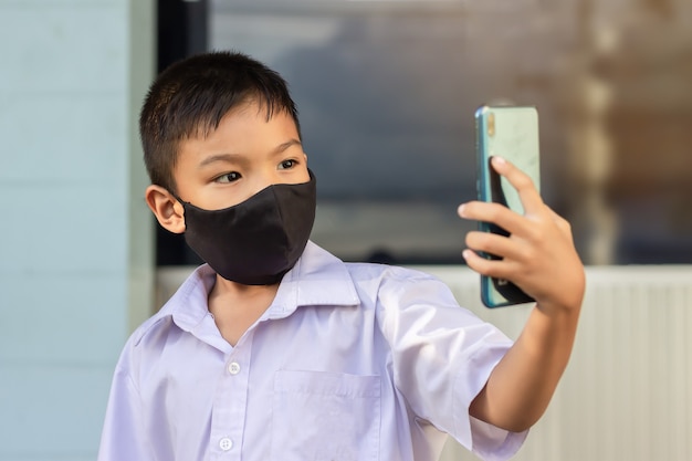 Asian child boy wearing black fabric mask on his face for prevent Covid-19 disease and corona virus.