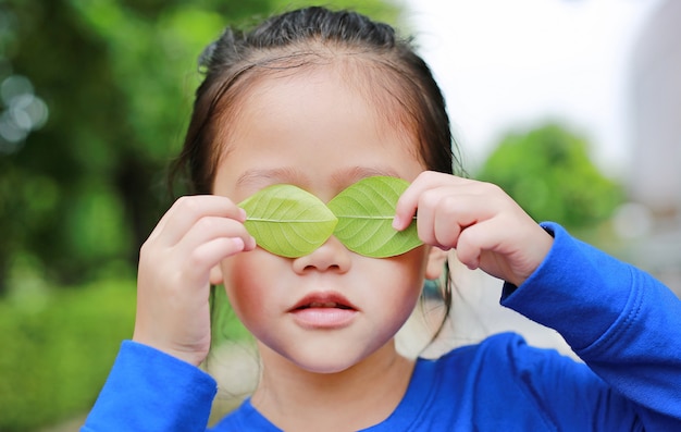 Asian child girl holding a green leaf closing eyes in green garden background.