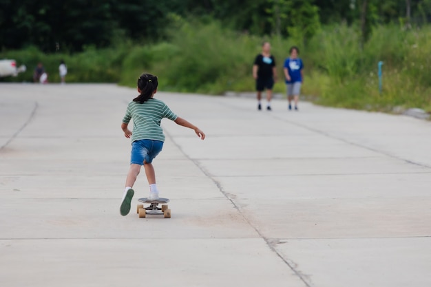 Asian child girl learning to skateboard outdoors. Kid having fun and playing skateboard on the road at the day time. Kid activity and extreme sport concept.