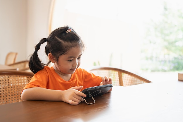 Asian child girl looking using and touch mobile phone screen Baby smiling funny time to use mobile phone Too much screen time Cute girl watching videos while tv Internet addiction concept